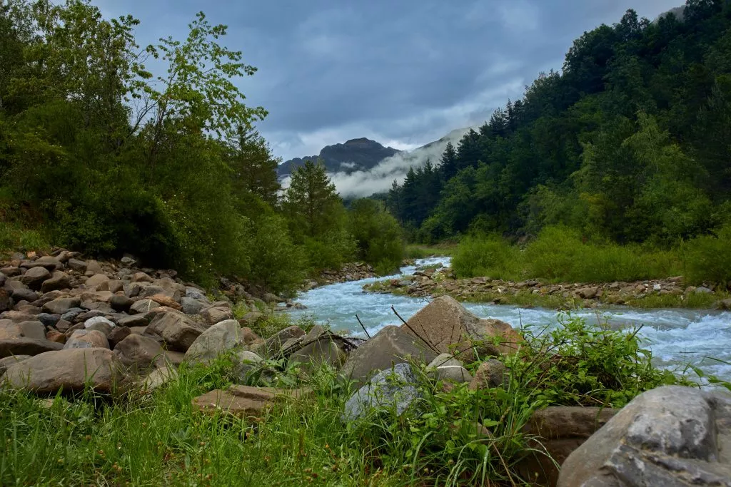 Mountain landscape with trees, clear water river and cloudy sky. Ara river in Huesca, Spain